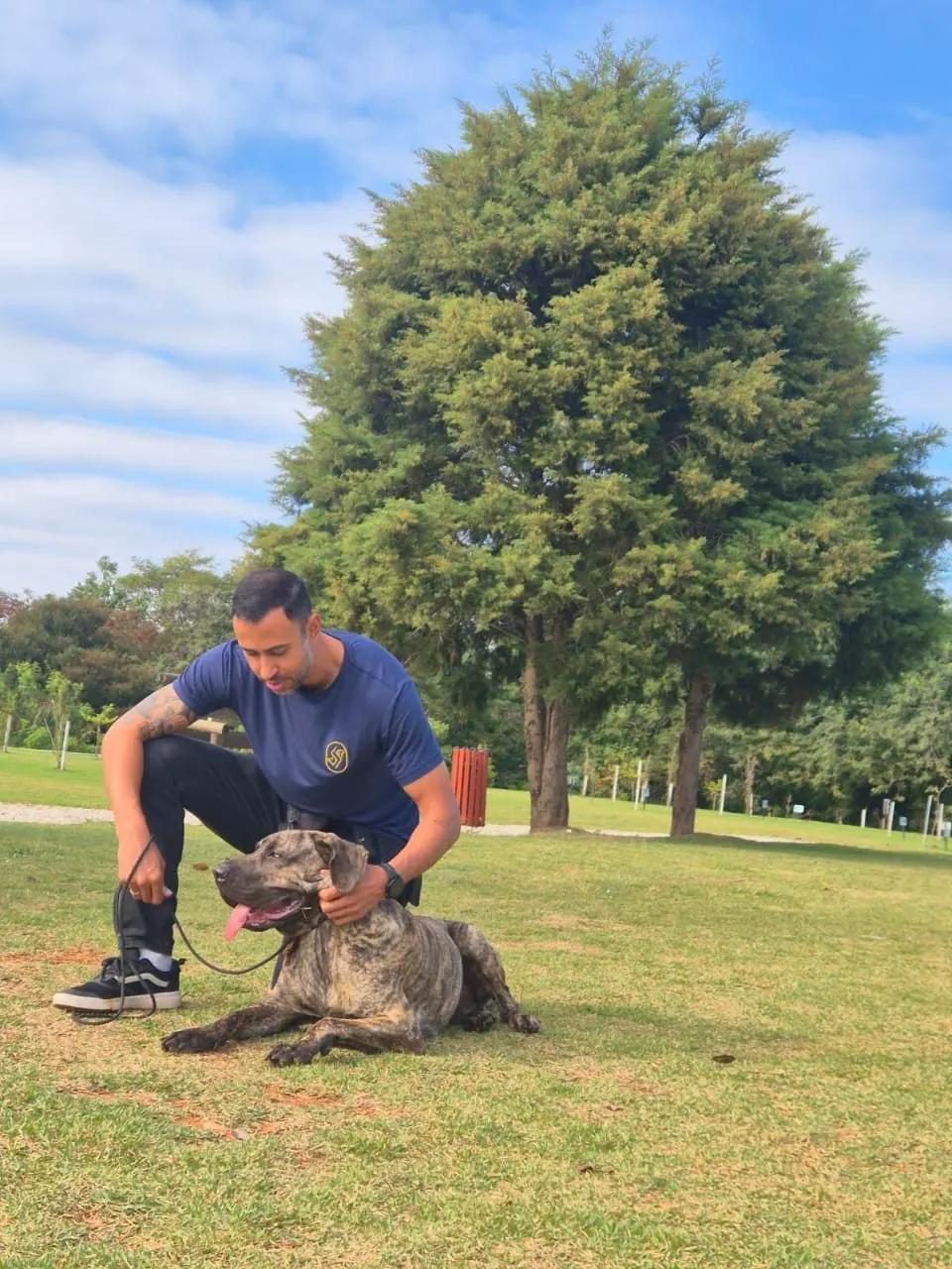 Ricardo agachado no parque com um cão deitado ao lado